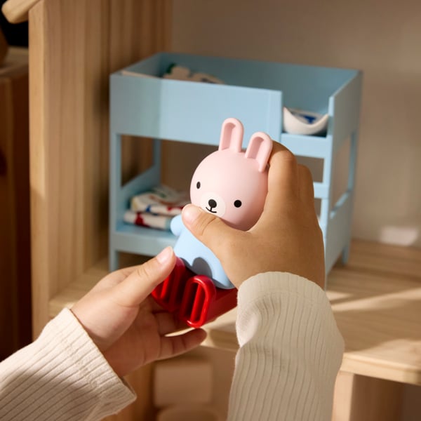 Gros plan sur les mains d’un enfant jouant avec des personnages et des meubles HUSET dans une maison de poupée FLISAT.