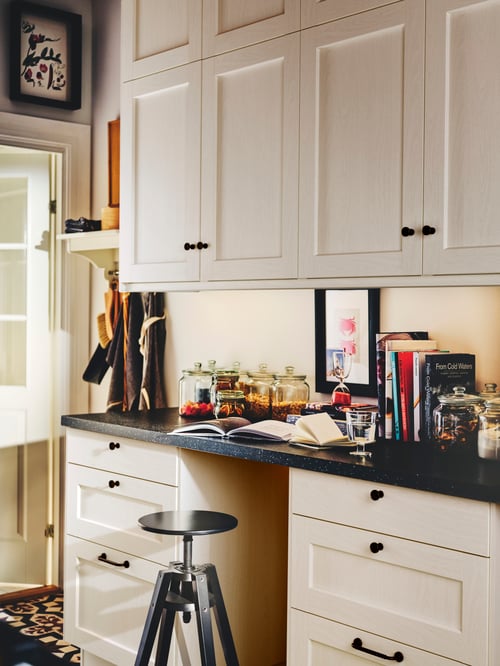 Kitchen with multiple white door made of fibreboard matching multiple white drawer fronts, placed next to a black bar stool.