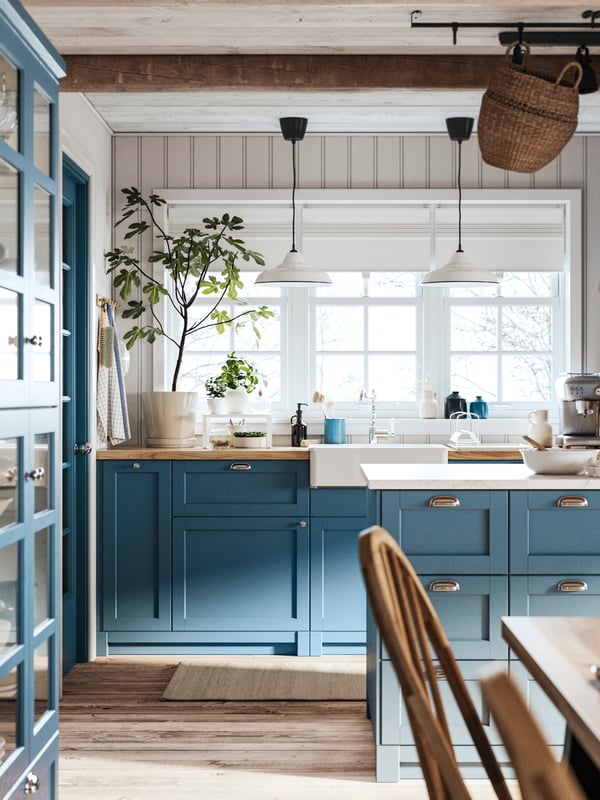 Une cuisine traditionnelle SEKTION avec des façades bleues LERHYTTAN, où les casseroles et les poêles sont accrochées à un rail mural.