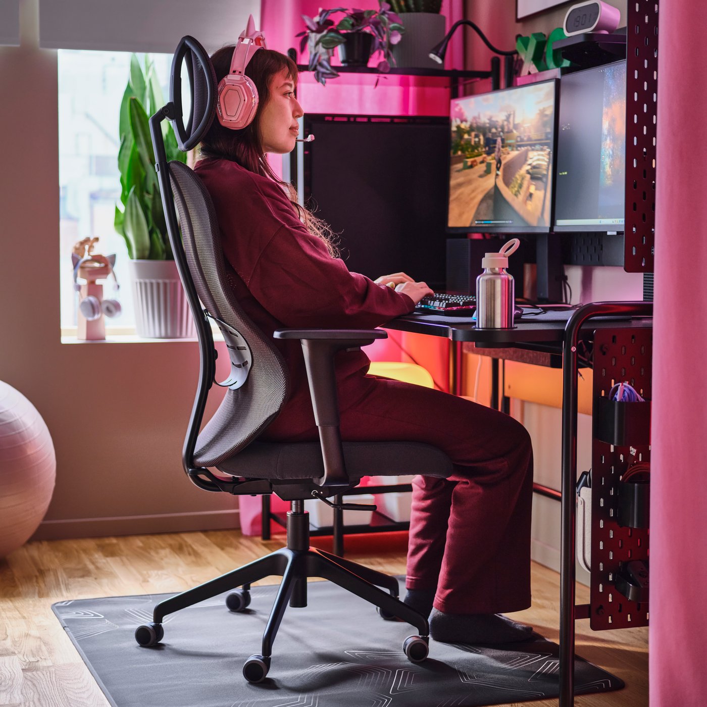 Una adolescente sentada en una estación de juego con una silla gamer UTKLASSNING en antracita y negro y un escritorio gamer FRÖSKELÅS negro.