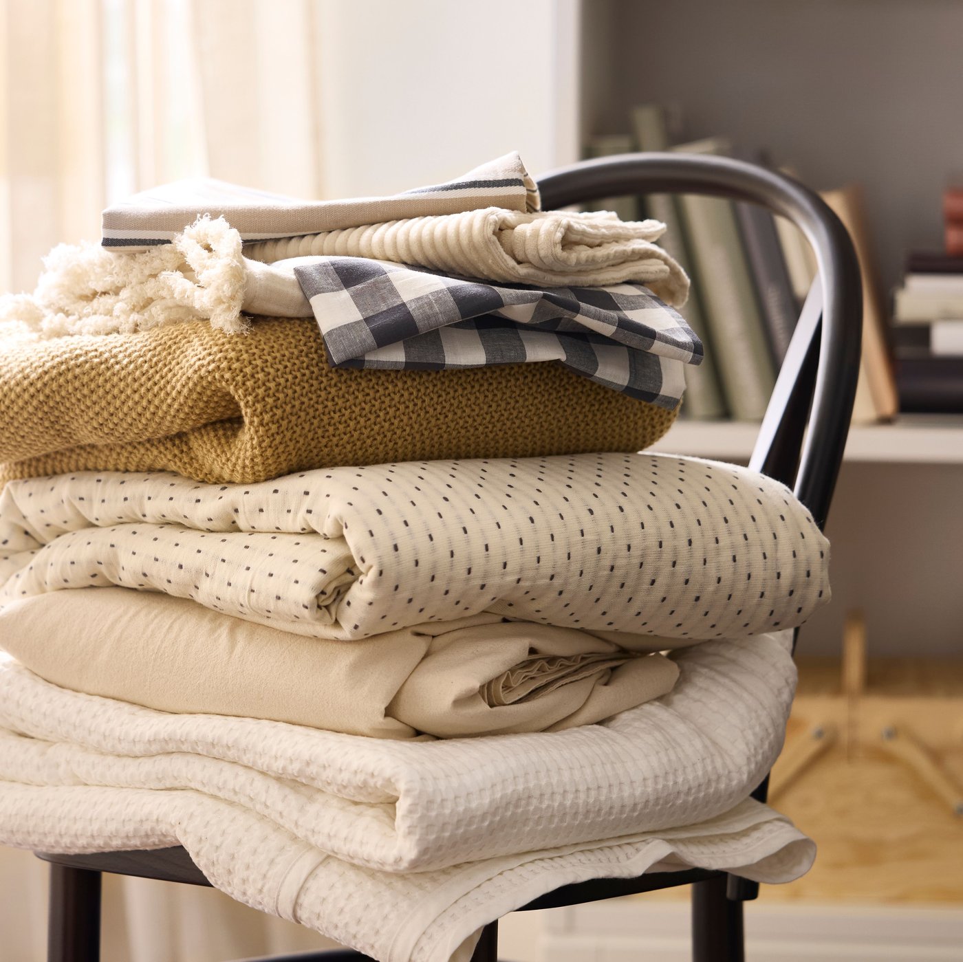 Tessili beige, bianchi e gialli impilati su una sedia SKOGSBO marrone scuro.