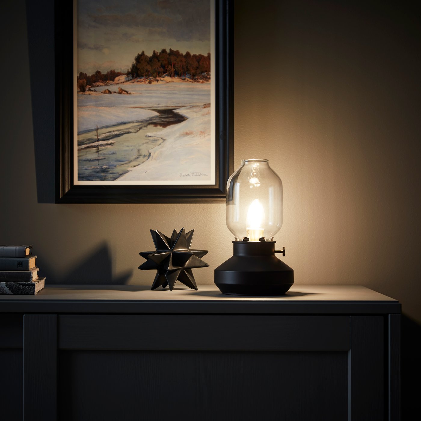 T: A warmly lit nightstand with a lamp and framed artwork, labeled “The Guiding Light”