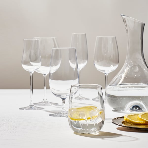 An assortment of IKEA STORSINT glasses in various sizes, a matching carafe on the side, on a white background.