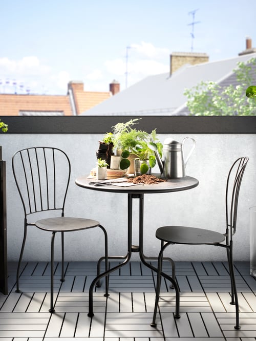 A terrace has a grey LÄCKÖ outdoor table and two chairs. On the table are seedlings, a watering can and potted plants.