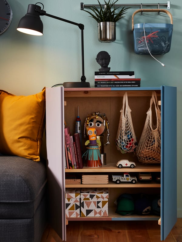 An open cabinet in a living room revealing two net bags, several small boxes and toys.