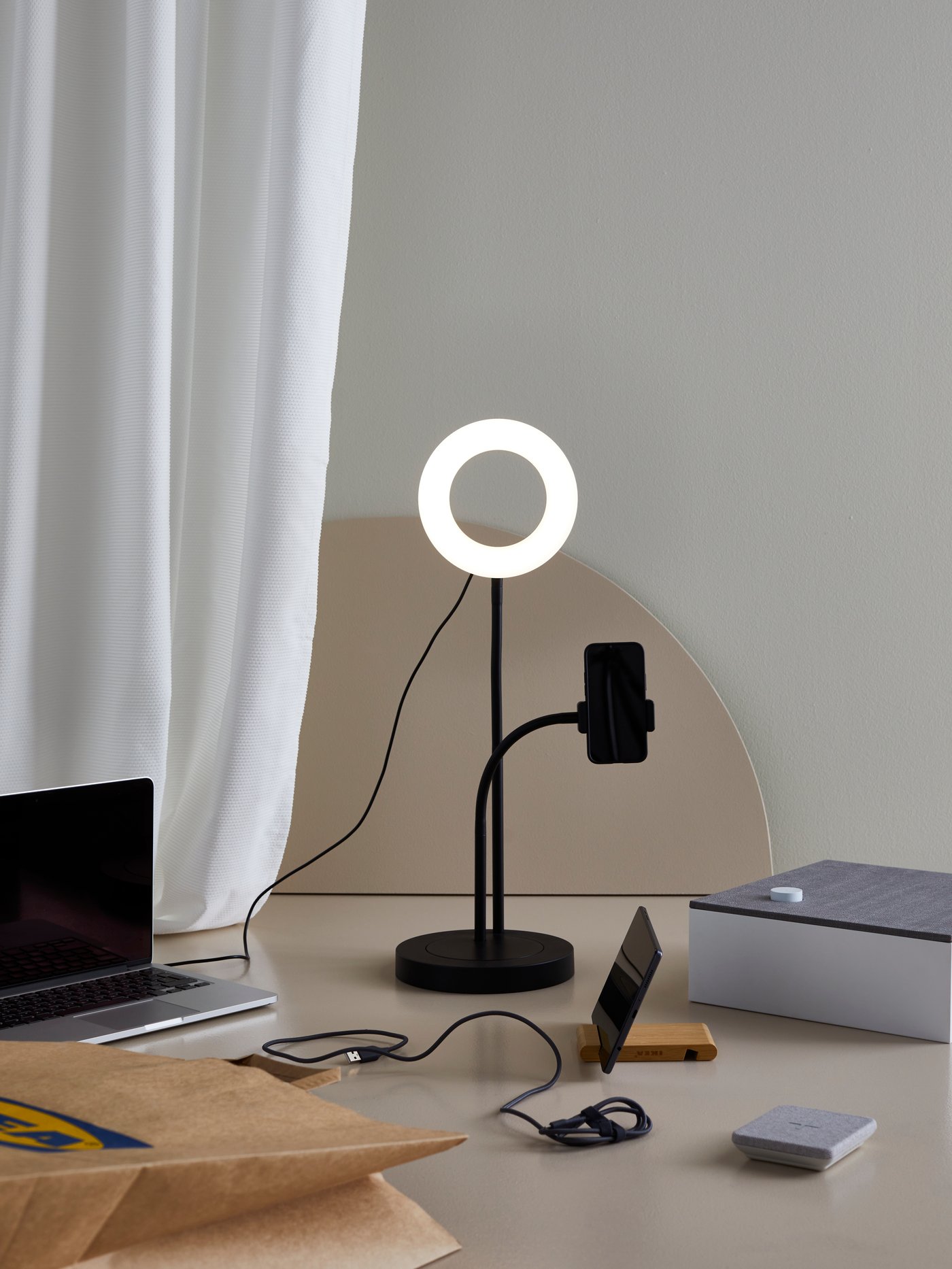 Sprzęt elektroniczny, w tym lampa pierścieniowa LÅNESPELARE, uchwyt na tablet BERGENES i głośnik Bluetooth ENEBY leżą koło siebie.
