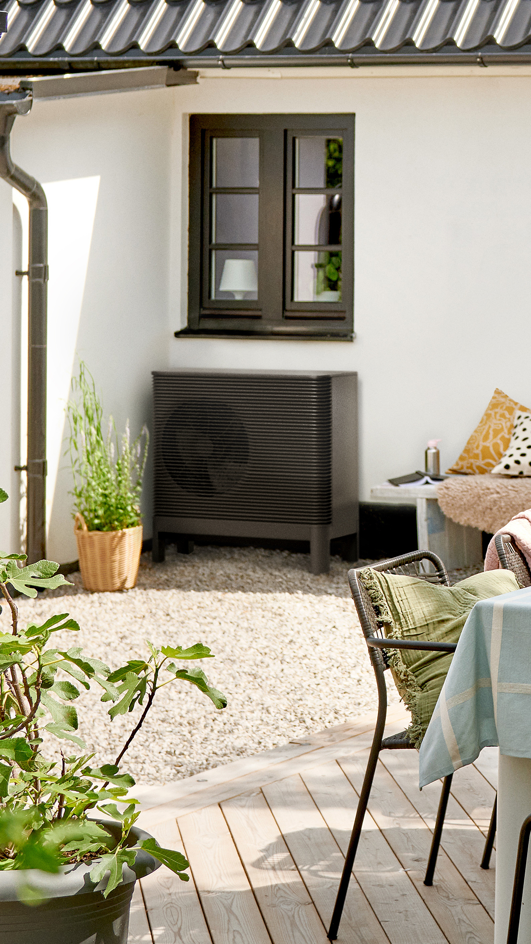 Ein Haus von außen, davor steht ein Tisch mit Stühlen und an der Wand ist eine Luft-Wasser Wärmepumpe zu sehen.