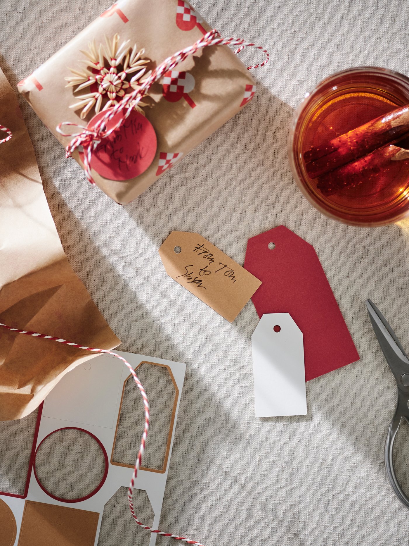 Weihnachtlich verpackte Geschenke mit Geschenkpapier, Geschenktüten, Anhängern und einer Tasse Punsch.