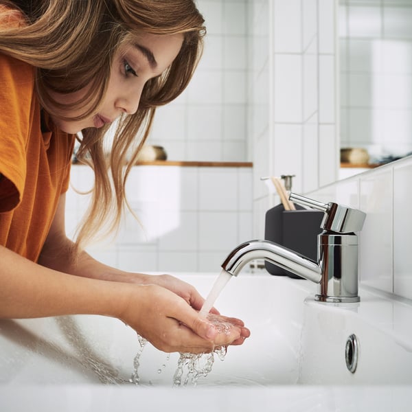 Una ragazza si china sul rubinetto dell'acqua e si riempie le mani d'acqua.