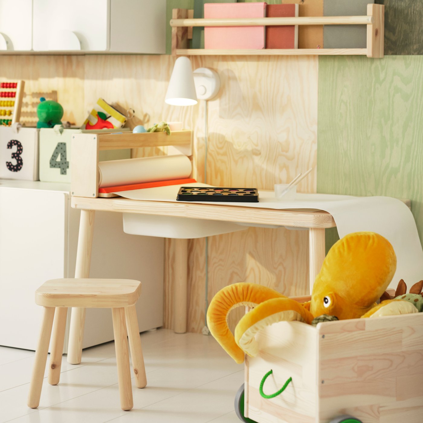 Barnrum med FLISAT skrivbord, stol och leksakslåda. På skrivbordet finns lampa, leksaker och rullpapper. I lådan ligger en stor gul bläckfiskmjukisdjur.