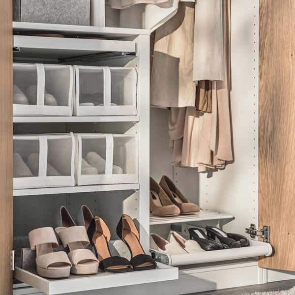 A white pull-out tray with shoe insert pulled out from a frame divider in a PAX wardrobe. Shelves above hold shoes in boxes.