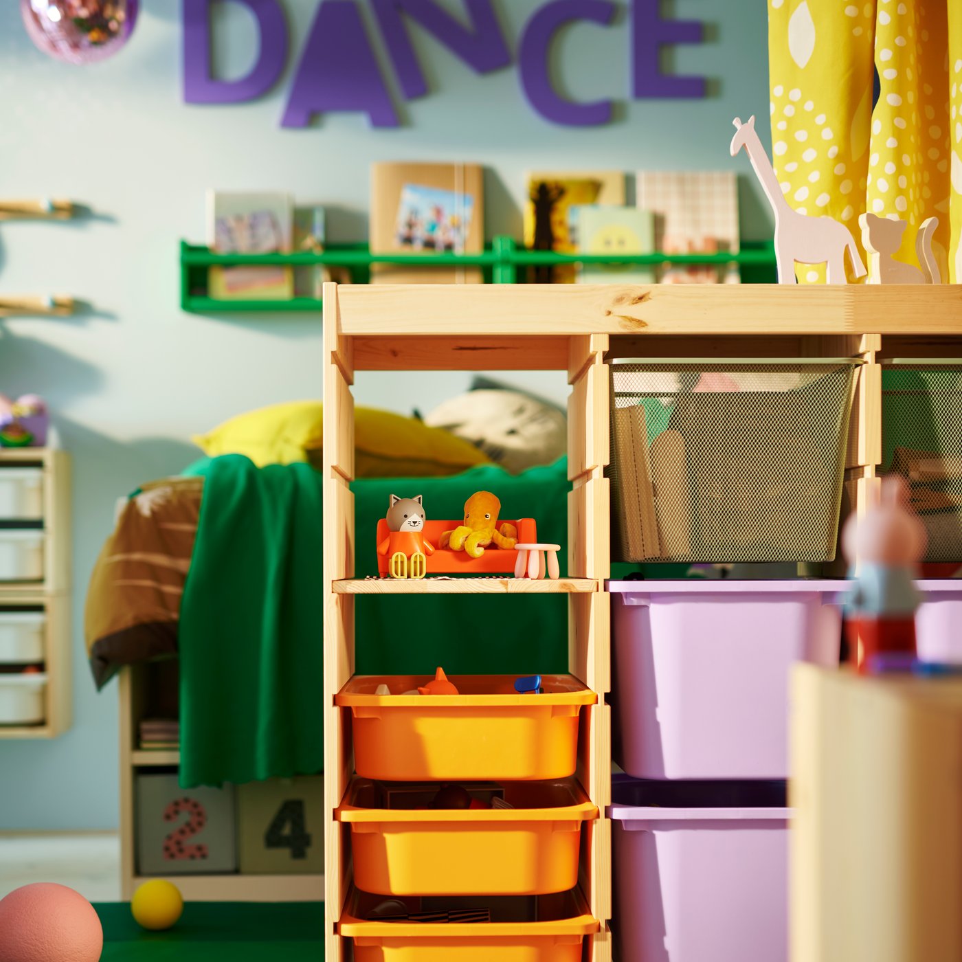 A TROFAST room divider in the middle of a children’s shared bedroom holding orange, lilac and mesh boxes, with toys on top.