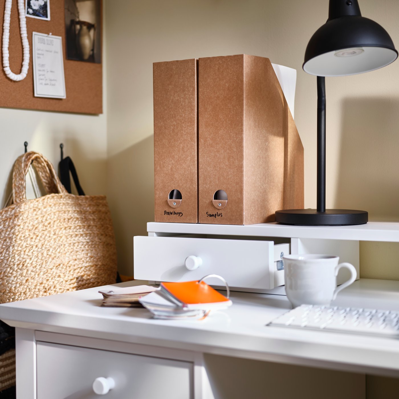 A white GULLABERG desk with an add-on unit with a drawer on top, scattered desk accessories, magazine files and a desk lamp.