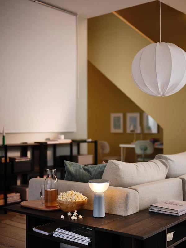 A yellow living room has a FRIDANS black-out roller blind on one wall, in front of a VIMLE 2-seat sofa and two side tables.