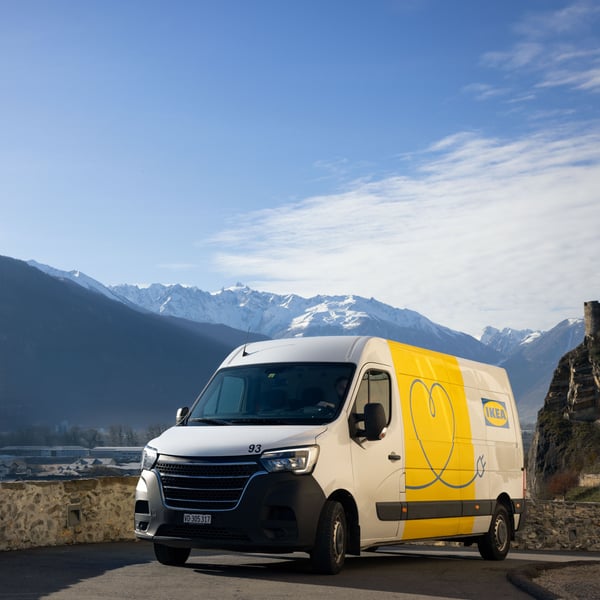 Un veicolo elettrico per le consegne IKEA su una strada in Svizzera, con il cielo azzurro e una catena montuosa parzialmente innevata sullo sfondo.