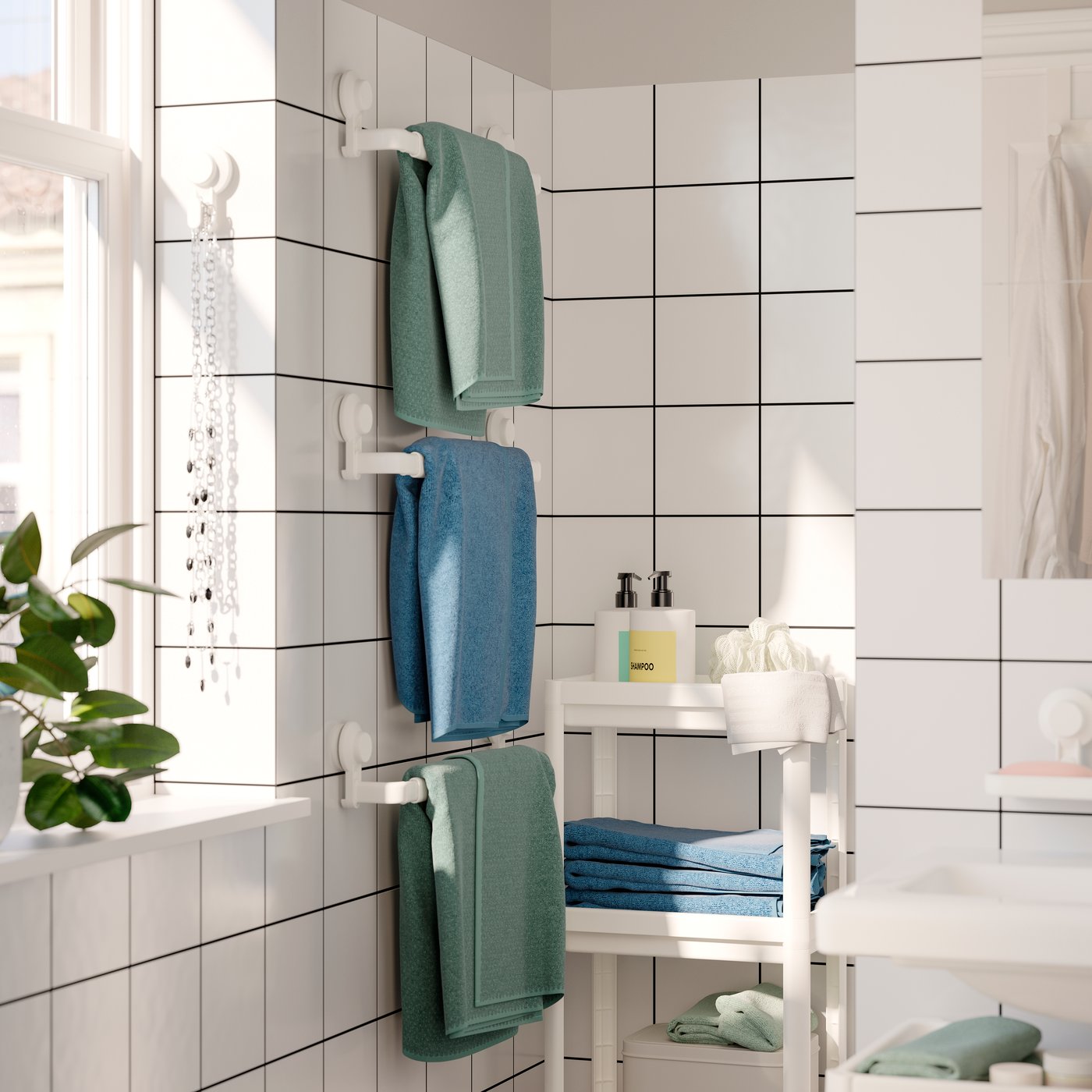 Drei Badetücher in gedecktem Grün und Blau hängen an drei TISKEN Handtuchhaltern mit Saugnapf. Weiss gefliestes Badezimmer.