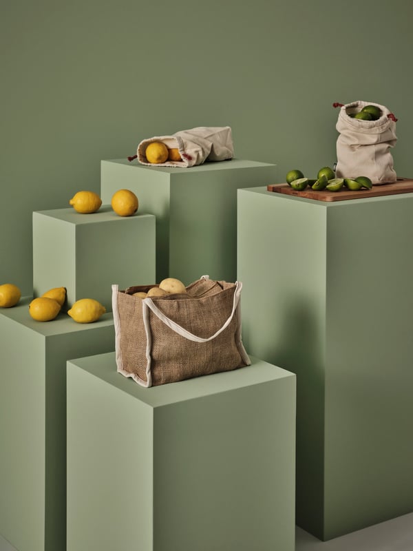 Three GULLRISMOTT food storage bags sit on green pedestals, with lemons, limes and potatoes inside and around the bags.