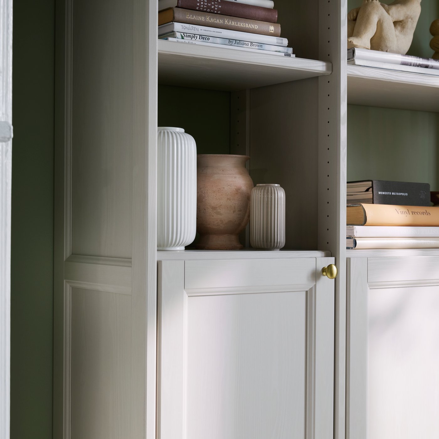 Close-up of the beige GULDDRAGARE storage combination with vases and books as decoration.