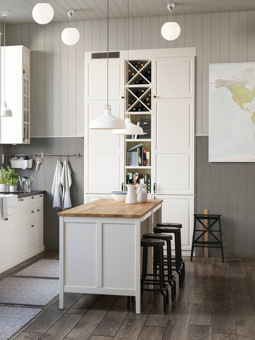 Kitchen with pendant lamp shades hanging over a kitchen island, with bar stools to the side and a stepladder in the back.