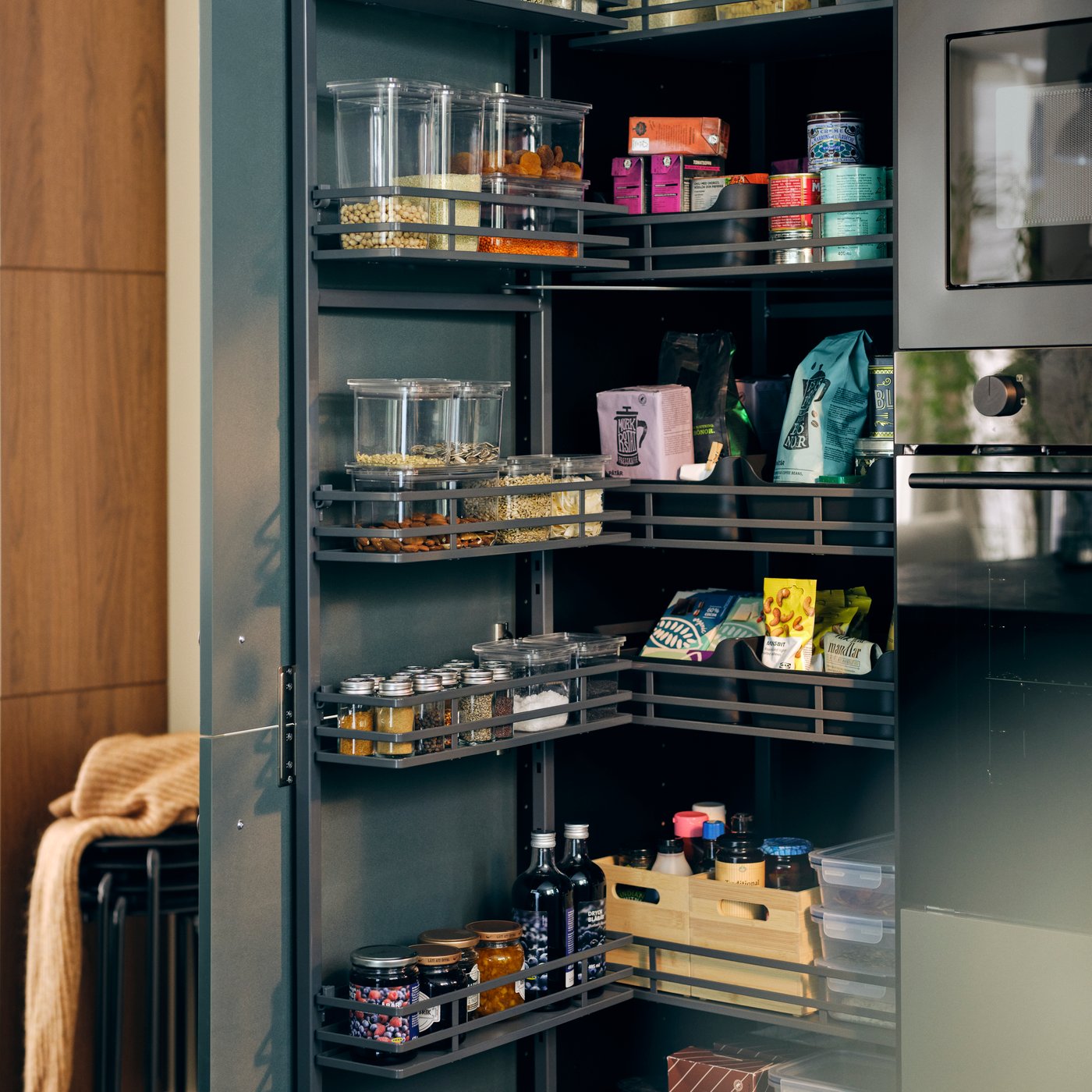 An UTRUSTA pull-out larder, the door is open to display shelves and baskets filled with food containers and diverse items.