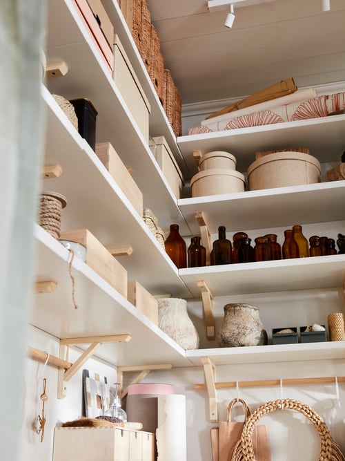 Living space with white shelves on the walls, personal belongings, storage boxes with lids, glass bottles, a ceiling lamp.