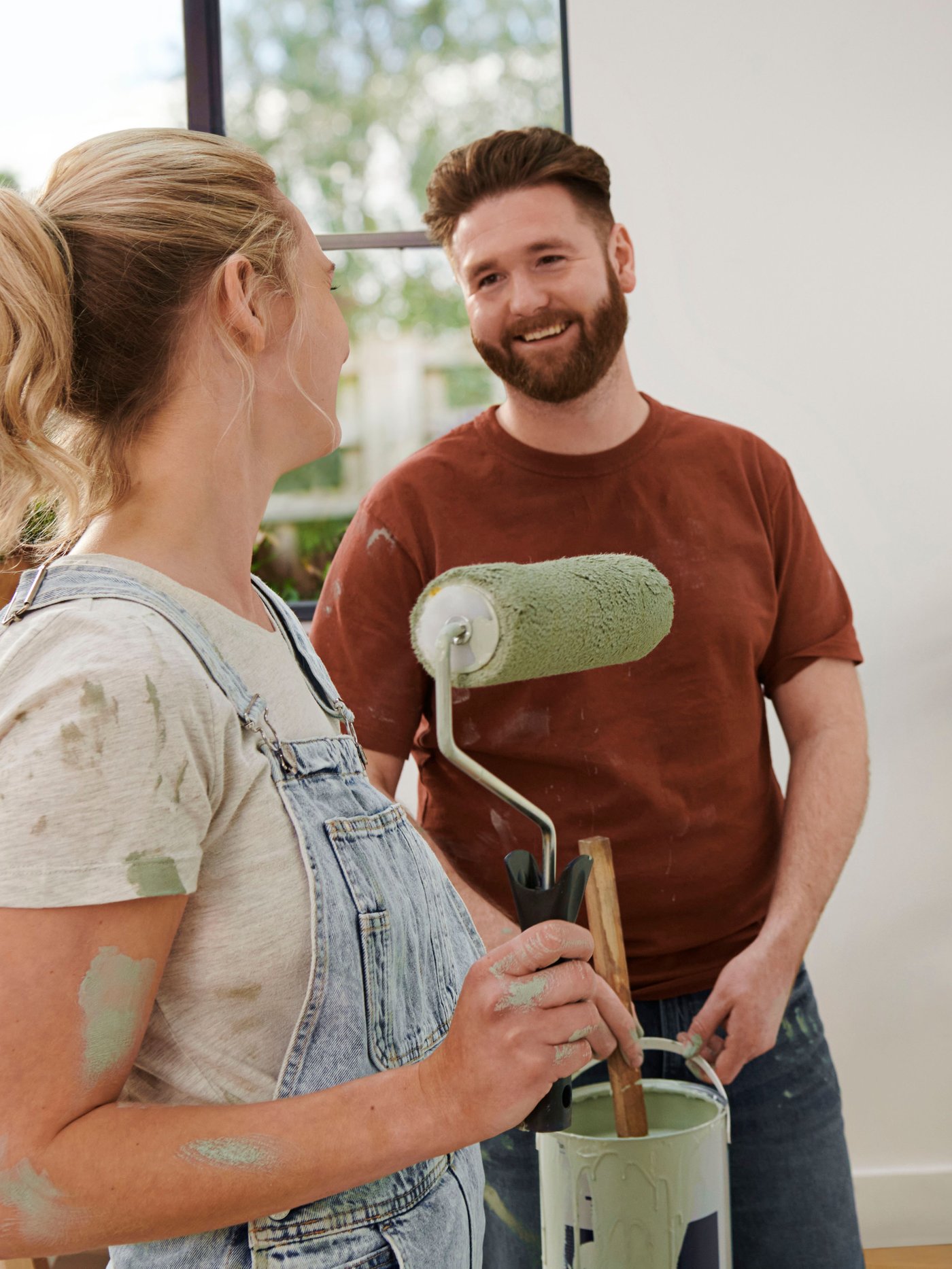 Zwei Personen mit Malerutensilien stehen in einem leeren Raum.