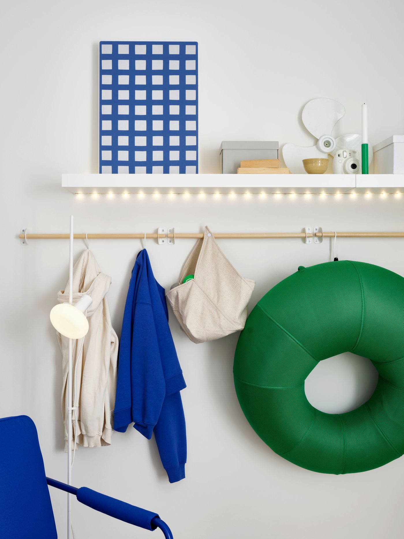 A white wall shelf with a SYMFONISK picture frame with speaker and ornaments on top, above an inflatable gaming chair hanging from a rail by a hook.