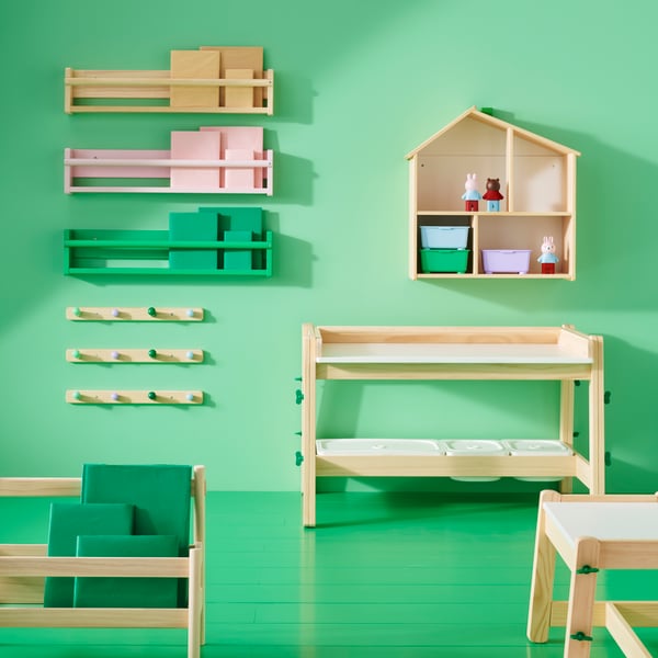 Verschiedene Artikel aus der FLISAT-Serie, darunter ein verstellbarer Schreibtisch und eine Bank, Wandregale und eine Garderobe in einem grünen Raum.