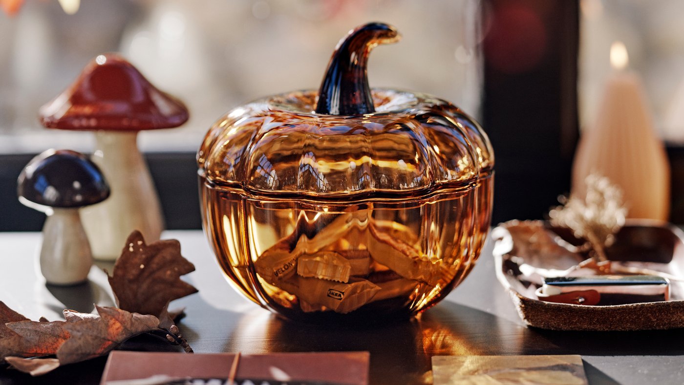 A brown HÖSTAGILLE pumpkin-shaped decoration bowl and lid filled with candy beside two HÖSTAGILLE decorative mushrooms.
