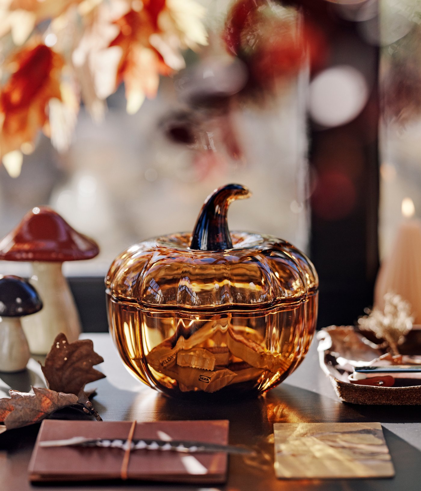 A brown HÖSTAGILLE pumpkin-shaped decoration bowl and lid filled with candy beside two HÖSTAGILLE decorative mushrooms.
