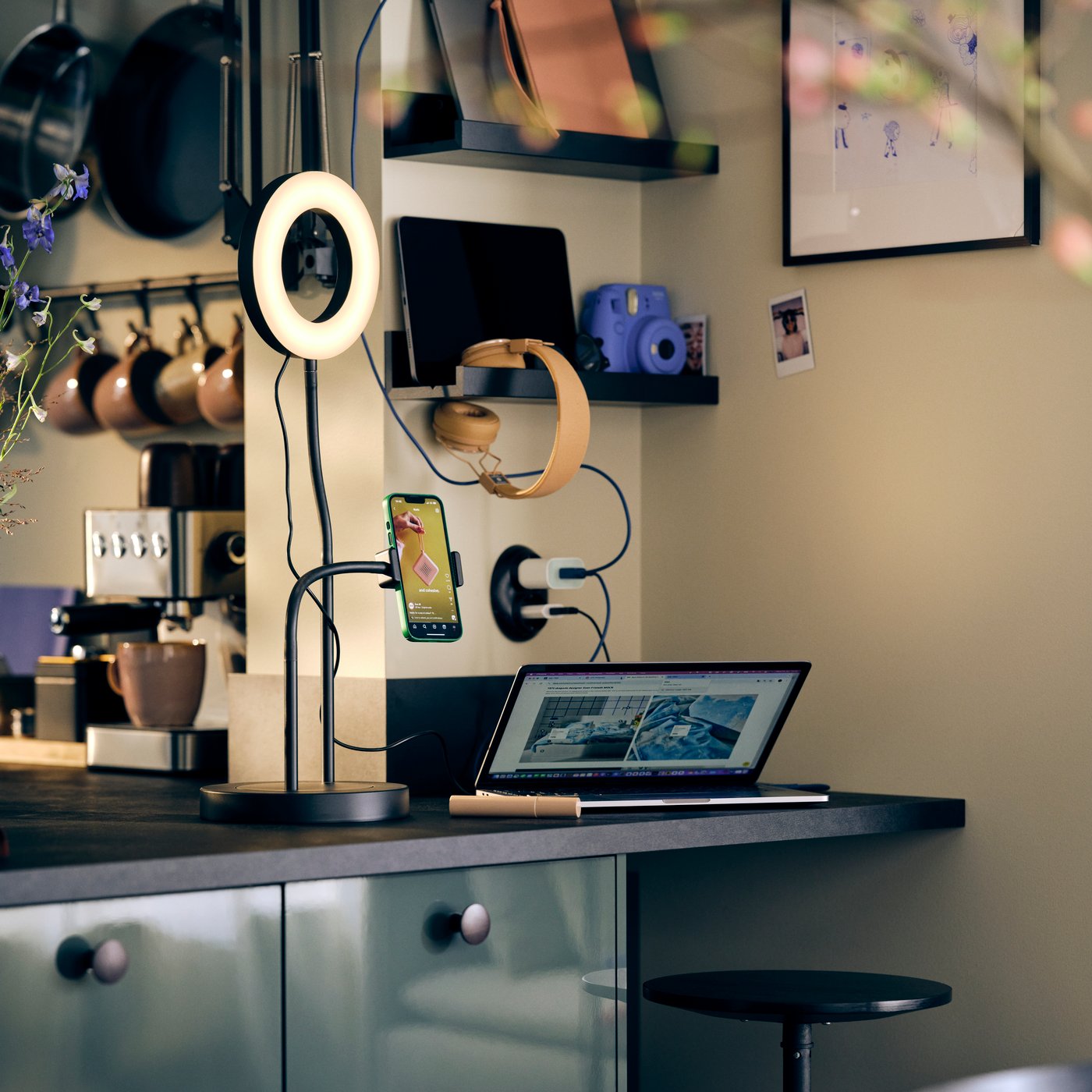 Ein gemeinsamer Ladebereich mit einem LÅNESPELARE Ringlicht mit Handyhalter, einem aufgeklappten Laptop und an der Wand hängenden Kopfhörern.