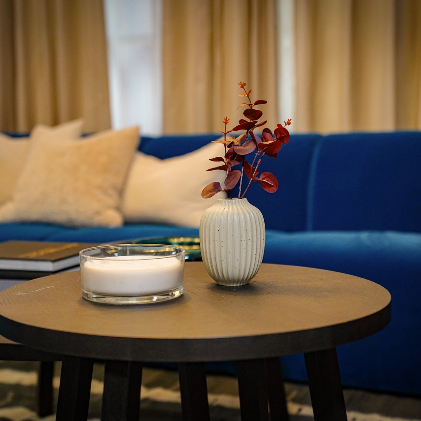 An oak veneer dark brown STOCKHOLM 2025 side table and dark brown STOCKHOLM 2025 coffee table in a room setting. LOTSFAGEL candle with 3 wicks and a white STJARNLUDD vase are stacked on top of the table.