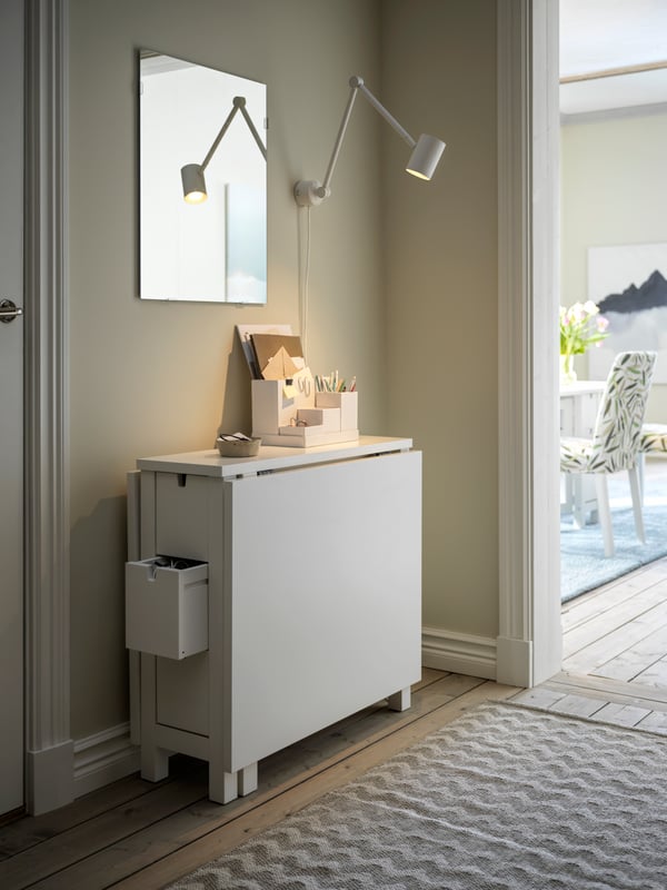 A hallway with a folded-down, white NORDEN gateleg table against a wall, and a LÄRBRO mirror a white NYMÅNE lamp above it.