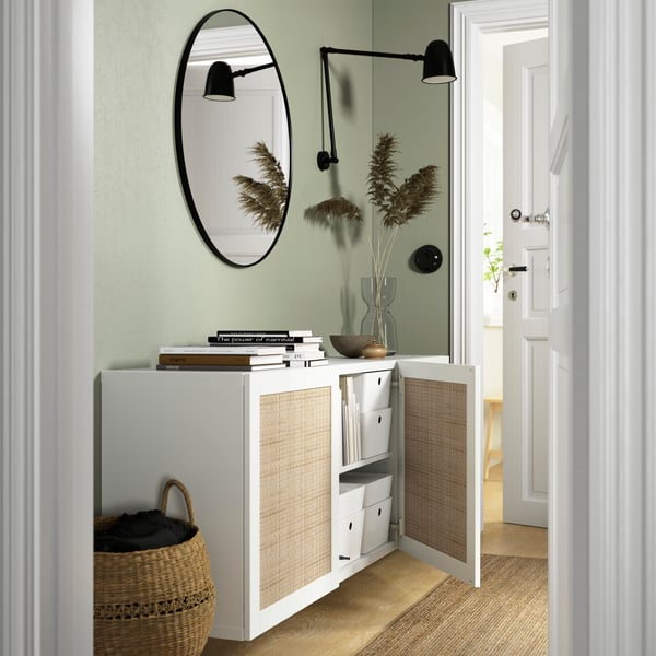 A BESTÅ storage combination with doors, white Studsviken. One door is open, displaying items inside. Above the unit is a LINDBYN round mirror.