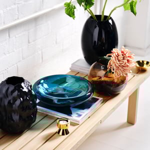 A blue-turquoise STOCKHOLM 2025 bowl next to a black organic vase, a brown STOCKHOLM 2025 vase, and a gold-colored STOCKHOLM 2025 tealight holder.