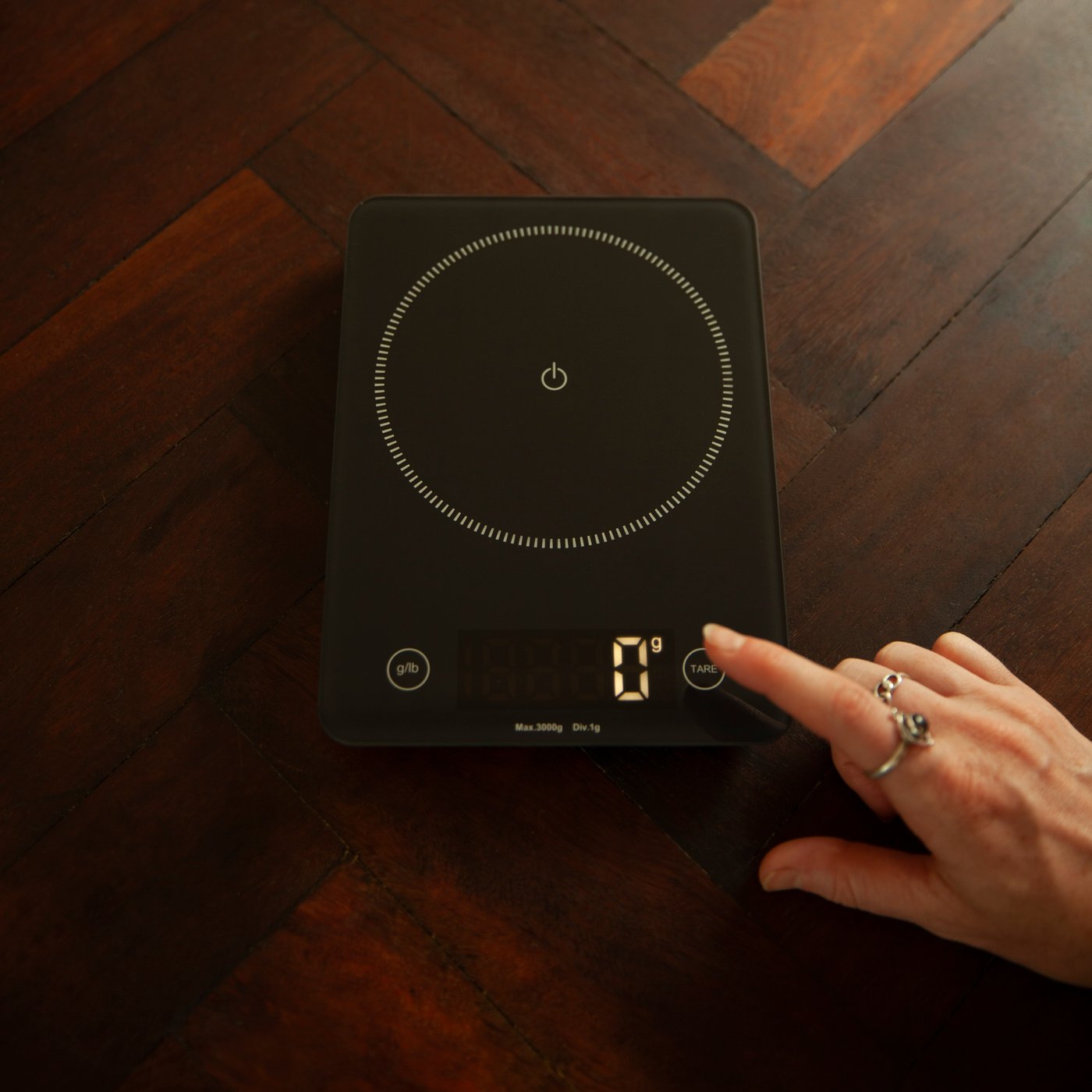 A hand turns on the GENOMSNITT electric scale.