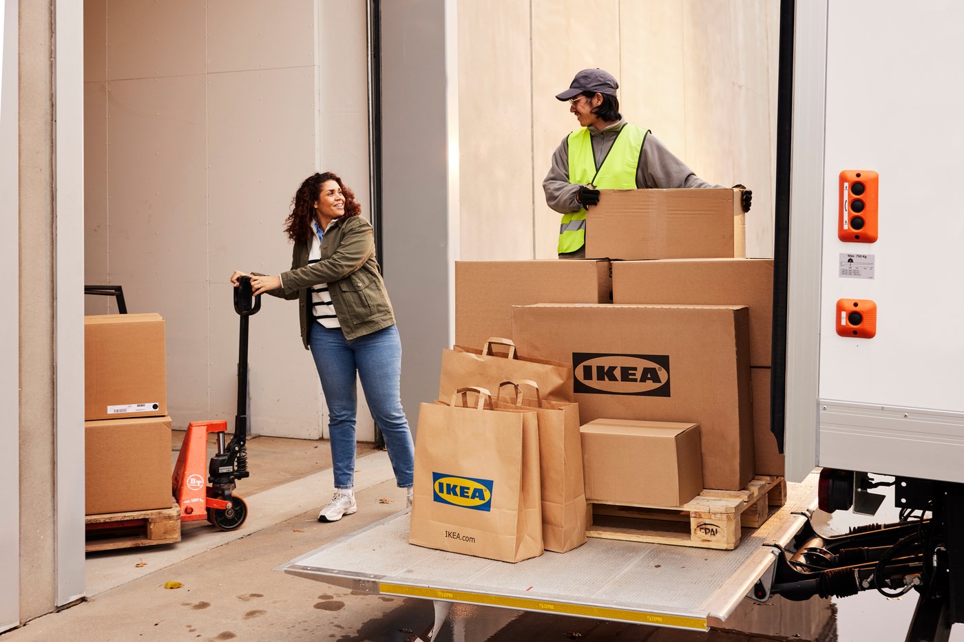 En lastbil lastar på eller av IKEA produkter. En kvinna står med en handtruck bredvid.