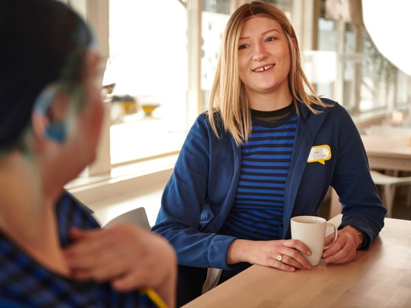 To IKEA medarbejdere, der er iført IKEA personaleuniformer, nyder en kop kaffe sammen i personalets kantine.