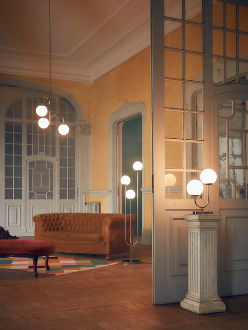 Modern living room with 3-armed pendant lamp, floor lamp, table lamp, coloured flat woven rug, a sofa.