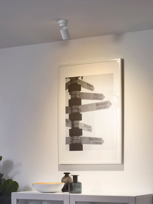 A NYMÅNE ceiling spotlight with 1 spot is mounted to the ceiling and shines its light on a poster on a wall.