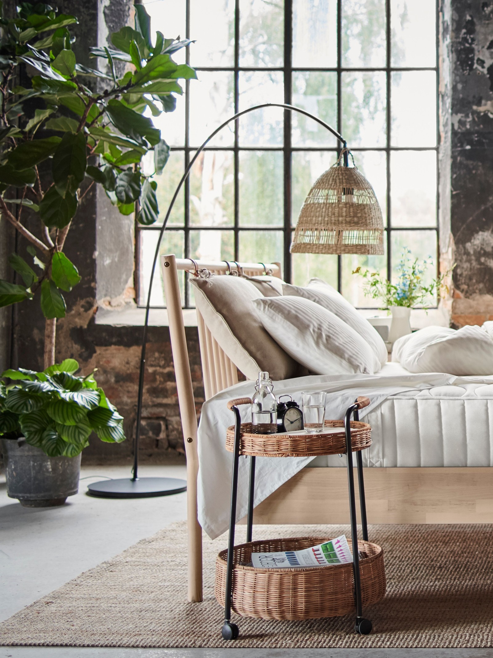 Un cadru de pat BJÖRKSNÄS într-un spațiu deschis, cu o măsuță de cafea și plante în fundal