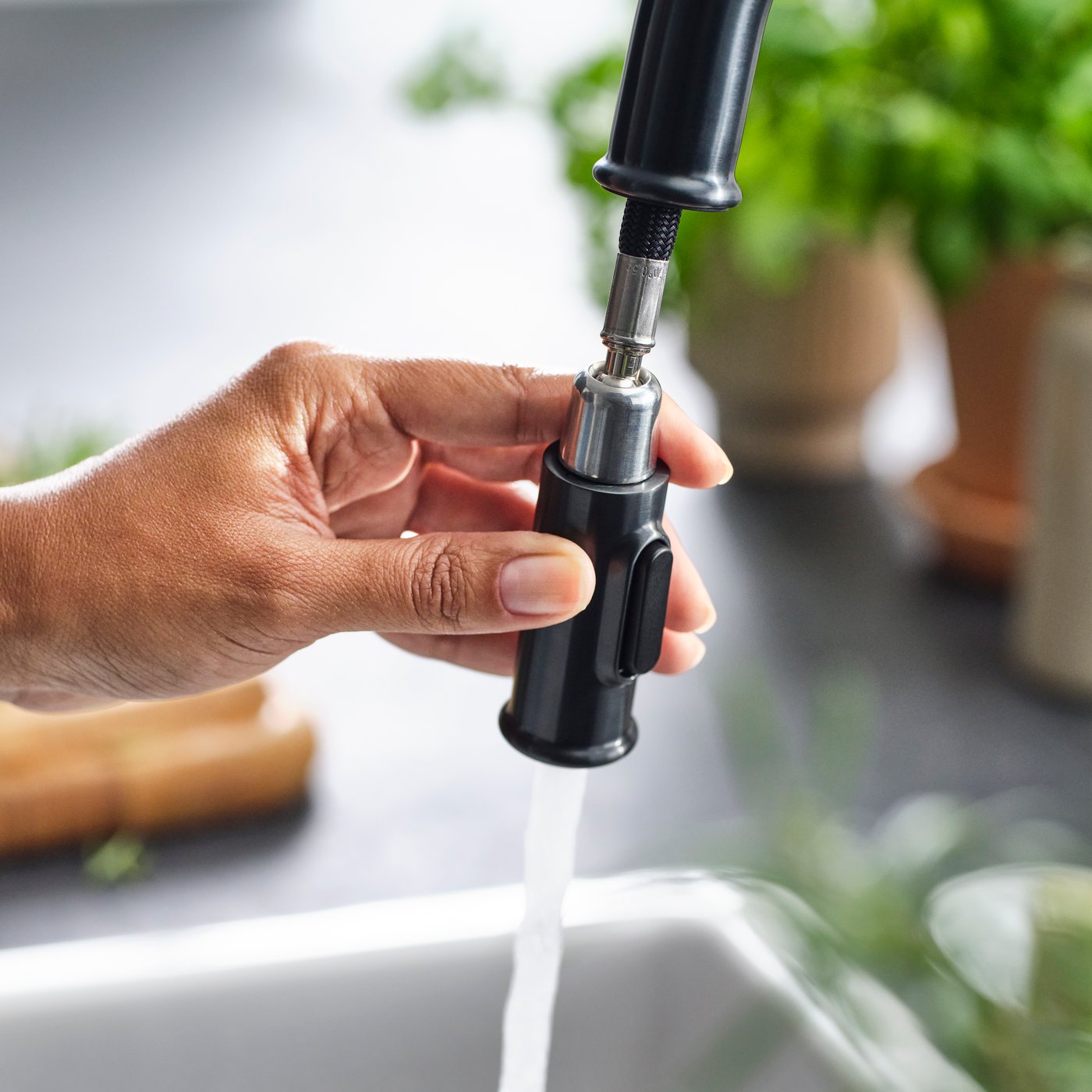 Close-up of a black TAKSJÖN mixer tap, as a hand uses the pull-out function and shows the spray button.