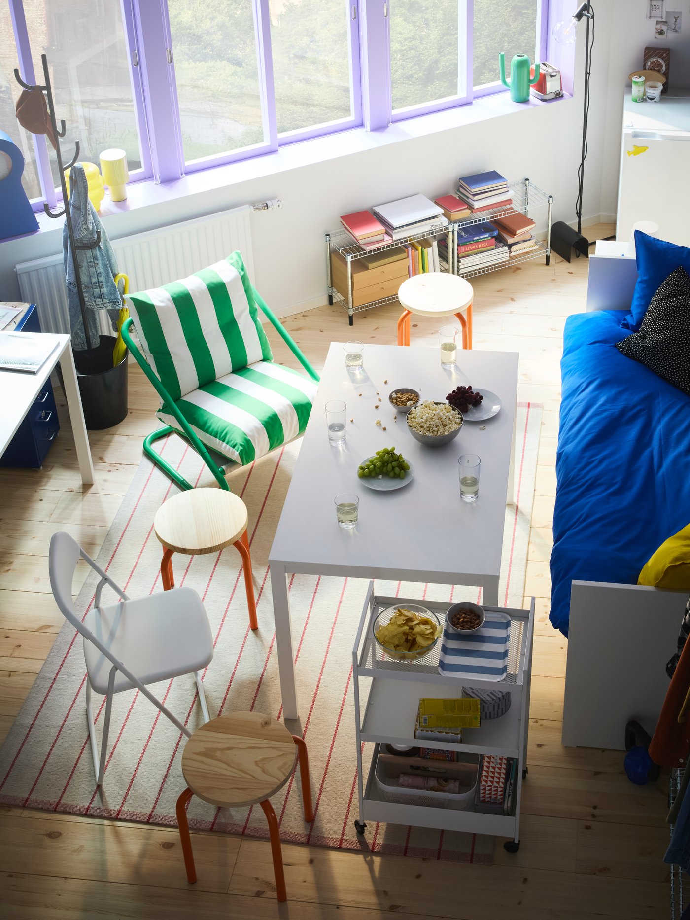 صورة من الأعلى لغرفة بها سرير نهاري وطاولة بها مقاعد منوعة وكراسي حولها نوافذ كبيرة في الخلف