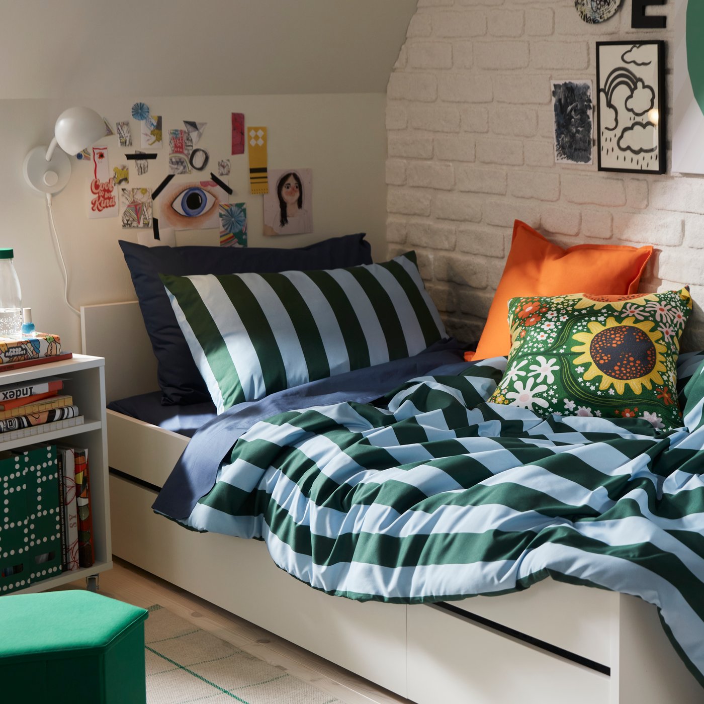 A bedroom with dark green and light blue striped SLÅNHÖSTMAL bedlinen on a white bed by a white brick wall.