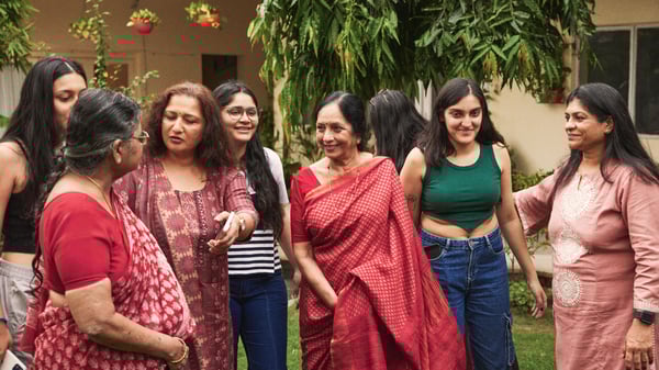 A group of women are standing in a garden in colorful clothes and socializing.