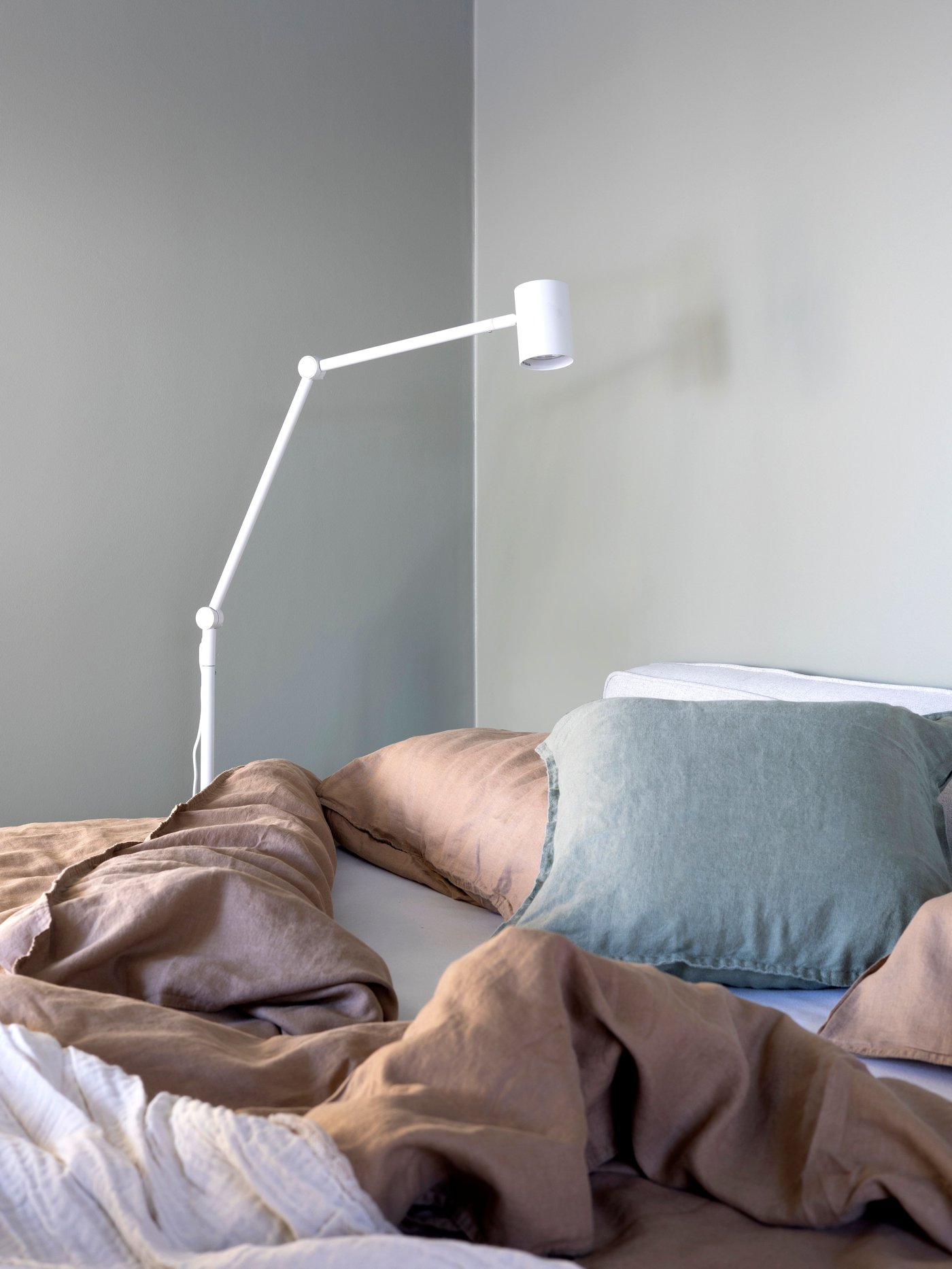 Lampadaire blanc sur le côté droit d'un lit défait.