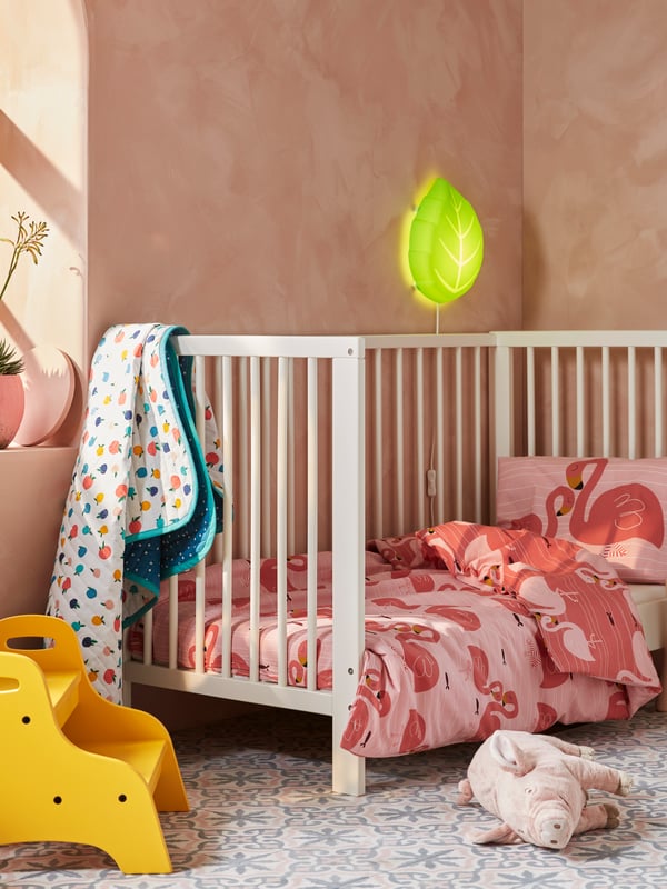 천연 텍스타일 러그와 바구니가 있는 화이트 마룻바닥 방의 IKEA SOLGUL 솔굴 유아용 침대에 누워 있는 아기.