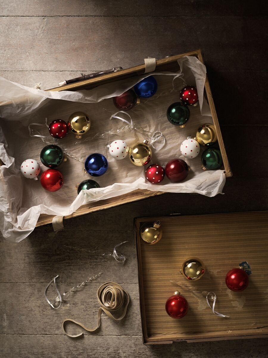 A selection of shiny baubles in blue, white, red, green and gold spread inside the lid of a brown cardboard box.