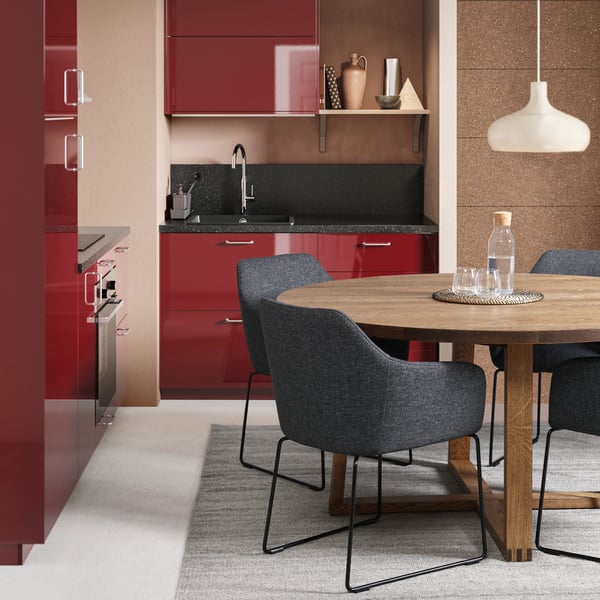 A red kitchen with a round wooden dining table and four grey TOSSBERG dining chairs.