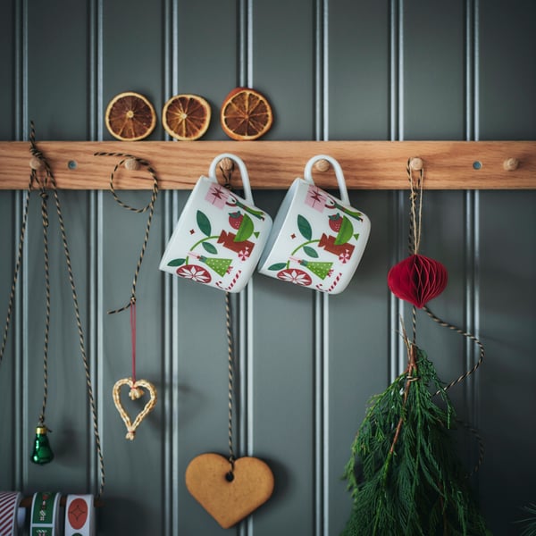 Des tasses VINTERFINT et des décorations festives suspendues sur une patère en bois